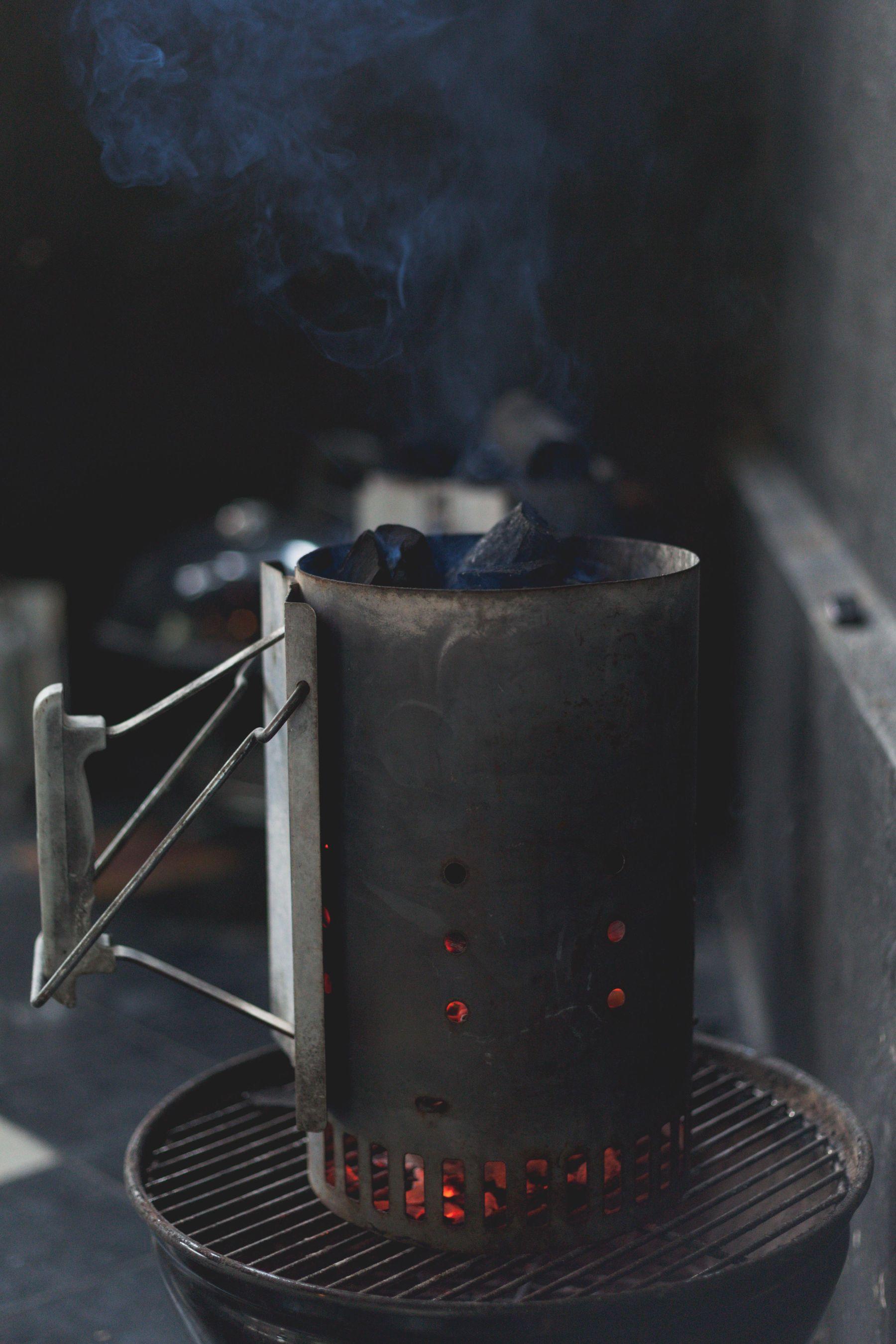 Charcoal chimney starter glowing on a grill grate with smoke rising